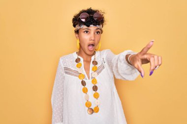 Genç ve güzel Afro-Amerikan Afro-Amerikan kadın güneş gözlüğü ve aksesuar takıyor. Parmağıyla işaret ediyor. İleride şaşırmış, ağzı açık, şaşırmış, ön tarafta bir şey var.