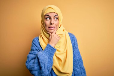Genç, güzel, esmer, Müslüman kadın izole edilmiş sarı arka plan üzerine Arap başörtüsü takıyor. Bir soru hakkında endişeleniyor, endişeli ve gergin.
