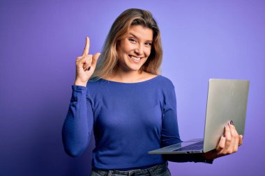 İzole edilmiş mor arka plan üzerinde dizüstü bilgisayar kullanan genç ve güzel sarışın kadın bir fikir veya soru işareti ile şaşırdı.