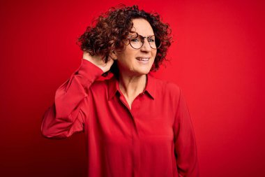 Orta yaşlı güzel kıvırcık saçlı kadın kırmızı arka planda gözlük takıyor ve dedikodu ya da dedikoduları dinlerken sırıtıyor. Sağırlık kavramı.