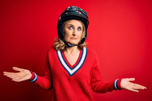 中世の美しいブロンドのオートバイの女性は 赤い背景の上に元ヘルメットを身に着けています 疑いの概念 — ストック写真