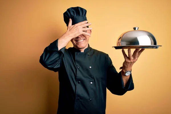 中世のハンサムな白髪のウエイター男性は 炊飯器の制服と帽子を保持トレイ笑顔を着て 驚きのために目をカバー顔に手で笑っています ブラインドコンセプト — ストック写真