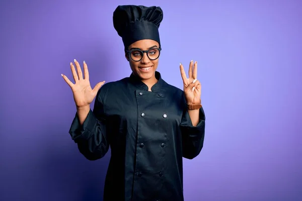 年轻的非洲女厨师身穿炊具制服 头戴紫色背景的帽子 带着八号手指 面带微笑 自信而快乐 — 图库照片