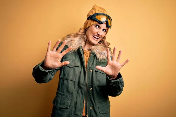 中年漂亮的金发碧眼的滑雪者女人穿着雪地运动鞋和滑雪护目镜 害怕而害怕 用恐惧的表情 用手停止手势 震惊地大叫 恐慌的概念 — 图库照片