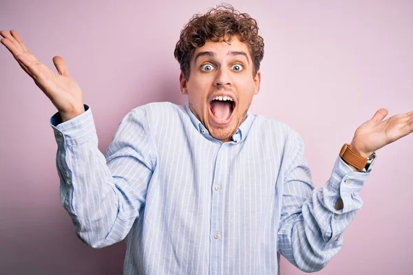 Sarışın, kıvırcık saçlı, beyaz arka planda çizgili tişört giyen, çılgın ve başarıyı kollarını kaldırıp heyecanla haykıran genç, yakışıklı bir adam. Kazanan konsept