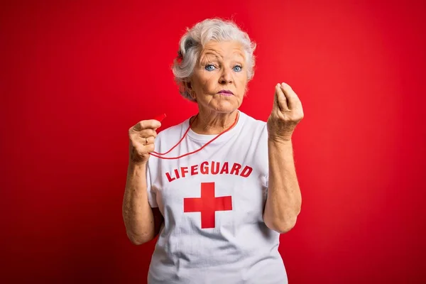 高级漂亮的灰白头发的救生员 身穿印有红十字图案的T恤 用哨子做意大利手势 手和手指都有自信的表情 — 图库照片