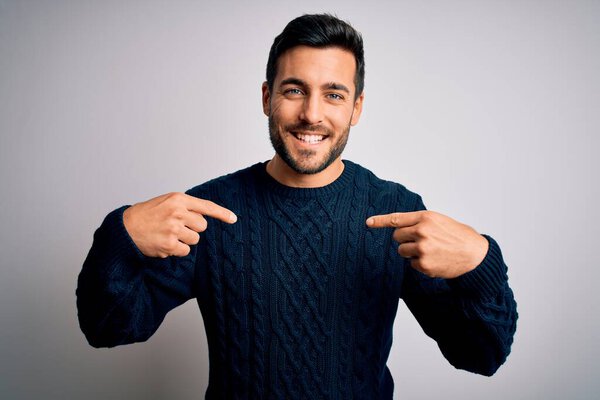 Young handsome man with beard wearing casual sweater standing over white background looking confident with smile on face, pointing oneself with fingers proud and happy.
