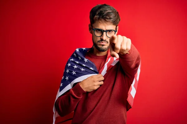 Young man wearing glasses and United States of America flag over isolated red background pointing with finger to the camera and to you, hand sign, positive and confident gesture from the front