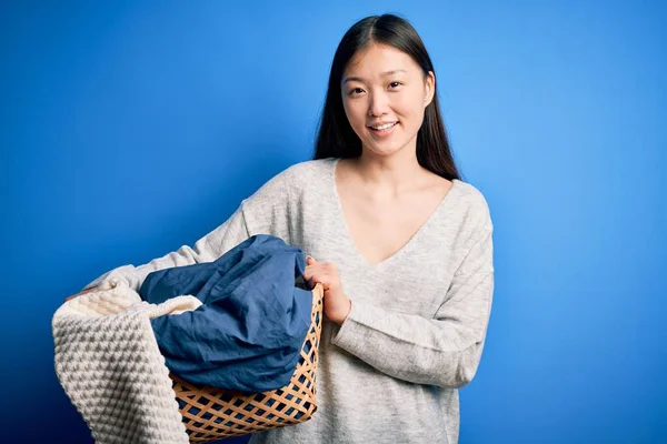 若いアジアの女性は 幸せな顔をした家事をし 歯を示す自信を持って笑顔で笑顔で洗濯バスケットを保持しています — ストック写真