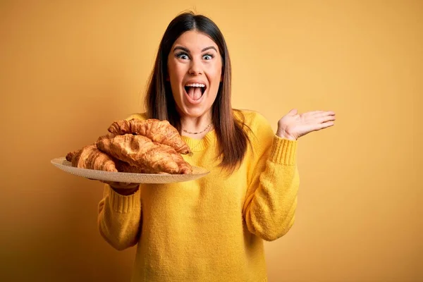 Młoda Piękna Kobieta Trzymając Francuskie Ciasto Croissant Żółtym Tle Bardzo — Zdjęcie stockowe