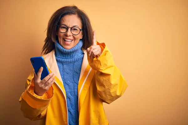 Frau Mittleren Alters Gelbem Regenmantel Mit Smartphone Über Gelbem Hintergrund — Stockfoto