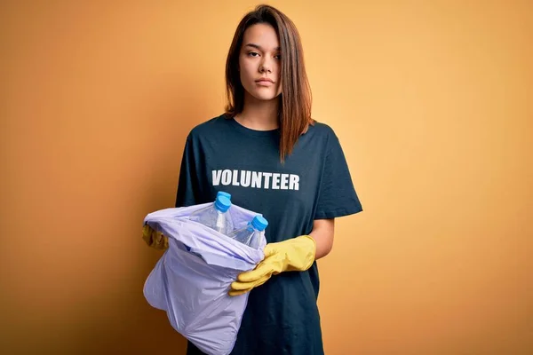 Beautiful volunteer girl caring environment doing volunteering holding bag with rubish bottles with a confident expression on smart face thinking serious