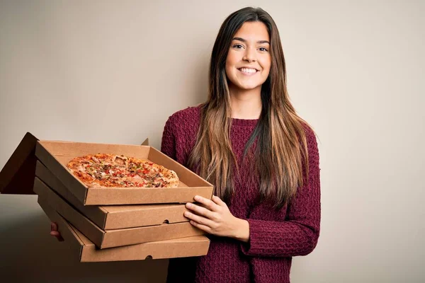 年轻美丽的女孩拿着装有意大利披萨的送货盒 站在白色的背景上 脸上挂着快乐的表情 脸上挂着自信的微笑 露出牙齿 — 图库照片
