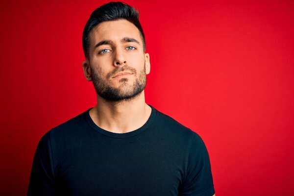 Young handsome man wearing casual black t-shirt standing over isolated red background Relaxed with serious expression on face. Simple and natural looking at the camera.