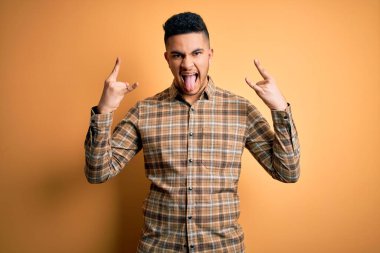 Sarı arka planda dikilmiş sıradan tişörtler giyen genç yakışıklı adam çılgın bir ifadeyle el kaldırarak rock sembolü yapıyor. Müzik yıldızı. Ağır müzik konsepti.