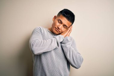 Genç, yakışıklı, latin kazaklı bir adam izole edilmiş beyaz arka planda dikiliyor. Yorgun uyuyor, hayal kuruyor, el ele poz veriyor ve gözleri kapalı gülümsüyor..