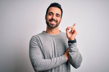 Sakallı, sıradan bir süveter giyen, yüzünde kocaman bir gülümsemeyle kameraya bakan, eli ve parmağı olan genç yakışıklı bir adam..