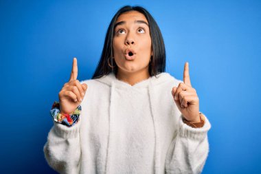 Eşofman üstü giyen Asyalı genç ve güzel bir sporcu. Mavi arka planda dikiliyordu. Şaşırmış ve şaşırmıştı..