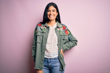 Moda kıyafetleri giyen genç ve güzel bir kadın. Manken, sokak tarzı giyiniyor. Pembe arka planda dikiliyor.