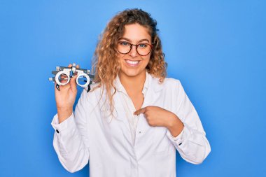 Gözü mavi olan güzel bir kadın izole edilmiş arka planda optometri gözlüğü tutuyor ve şaşırmış yüz ifadesi kendini gösteriyor.