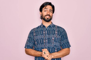 Pembe arka planda hippi tarzı giyinen genç, yakışıklı, bohem bir adam ellerini kavuşturup gülümsüyor. Başarı ve iyimser