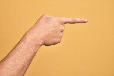 İzole edilmiş sarı arka plan üzerinde parmaklarını gösteren beyaz bir gencin eli işaret parmağıyla kenarı işaret ediyor ve bir seçim yapıyor.