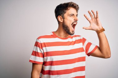 Beyaz arka planda duran çizgili tişörtlü, sakallı, genç ve yakışıklı bir adam el ele verip bağırıyor. İletişim konsepti.