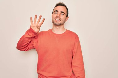 Mavi gözlü genç adam beyaz arka planda dikilip dört numarayı gösterirken kendinden emin ve mutlu bir şekilde gülümsüyor..