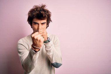 Genç ve yakışıklı bir adam pembe arka planda dikiliyor. Yumruk savunma hareketleriyle kavga etmeye hazır. Kızgın ve üzgün bir yüz, sorundan korkuyor.