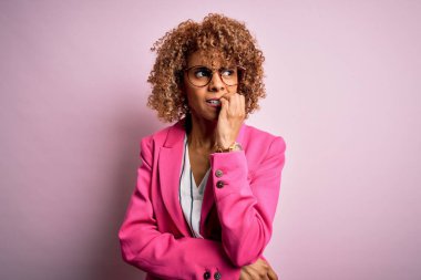 Genç Afro-Amerikalı iş kadını pembe arka planda duran gözlüklü gergin ve gergin görünüyor ve elleri ağızdan tırnak yiyor. Endişe sorunu.