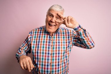 Üst düzey yakışıklı, parlak gömlekli, pembe arka planda yalnız başına barış sembolü çiziyor, parmakları yüzünde, neşeyle gülümsüyor, zaferini gösteriyor.