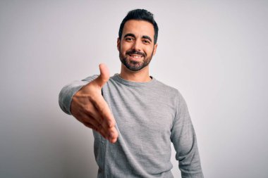 Sakallı, sıradan bir süveter giyen, beyaz arka planda duran yakışıklı genç bir adam dostça bir selamlama ve hoş geldin hediyesi olarak el sıkışma sunuyor. Başarılı bir iş..