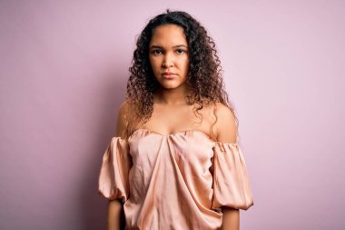 Kıvırcık saçlı, pembe arka planda sıradan tişörtler giyen genç ve güzel bir kadın. Yüzünde ciddi bir ifadeyle rahatlamış. Basit ve doğal bir şekilde kameraya bakıyorsun..