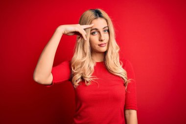 Ayrı kırmızı arka plan üzerinde dikilen sıradan tişörtlü genç, güzel sarışın kadın alnındaki sivilceden mutsuz olduğunu gösteriyor, siyah noktalı çirkin bir enfeksiyon. Sivilce ve deri problemi