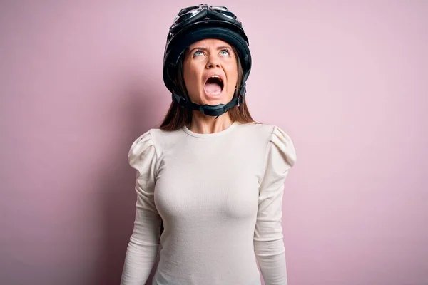 青い目をした若い美しいバイク乗りの女性は 怒りで叫んで ピンクの背景の怒りと怒りの上に元ヘルメットを身に着けています 激怒と積極的な概念 — ストック写真