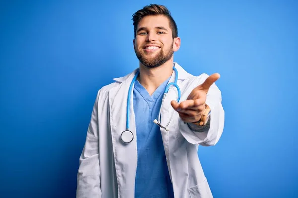 年轻的金发医生 留着胡子和蓝眼睛 身穿白衣和听诊器 微笑友善地握手致意和欢迎 成功的业务 — 图库照片