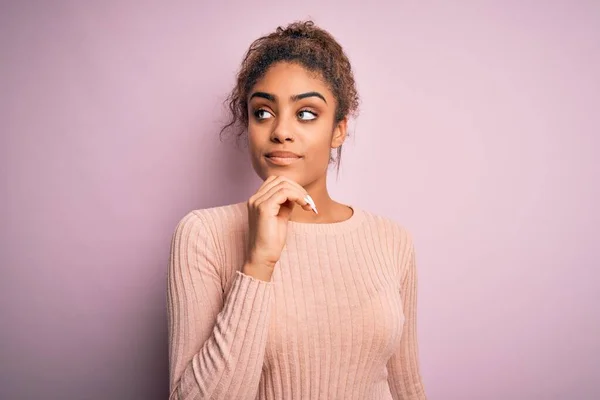 若い美しいアフリカ系アメリカ人の女の子がピンクの背景にピンクの背景に立ってカジュアルなセーターを着て あごの質問について考えて 集中的な表現 笑顔と思慮深い顔 疑いの概念 — ストック写真