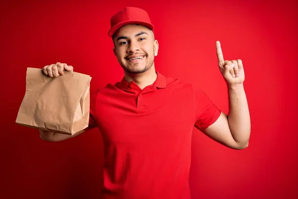 Kırmızı Arka Planda Paket Yiyecek Taşıyan Yakışıklı Teslimatçı Bir Fikir — Stok fotoğraf