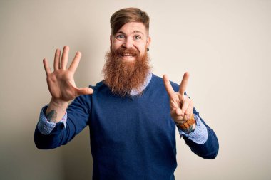 Yakışıklı, kızıl saçlı, sakallı bir iş adamı izole edilmiş arka planda duruyor ve yedinci parmaklarını gösterip gülümsüyor. Kendinden emin ve mutlu..
