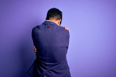 Ceket ve gözlük takan yakışıklı bir iş adamı mor arka planda mutlu ve pozitif bir şekilde kendine sarılıyor. Sevgi ve özgüven.