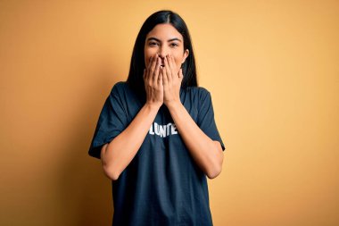 Sosyal yardım derneği ahlakı olarak gönüllü tişörtü giyen genç ve güzel İspanyol kadın gülüyor ve kıkırdıyor elleri, dedikoduları ve skandalları ağızlarına tıkıyor.