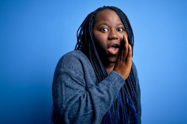 Afro-amerikan kadın örgü örüyor mavi arka planda kazak giyiyor gizli dedikodular söylüyor, kötü niyetli konuşmalar fısıldıyor.