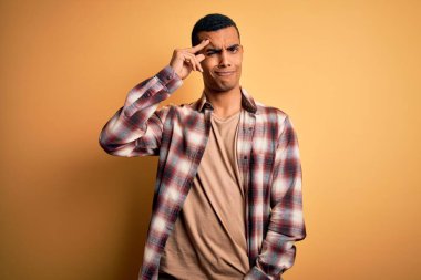 Sarı arka planda dikilen rahat gömlekli, genç ve yakışıklı Afro-Amerikan adam. Alnındaki sorun yüzünden endişeli ve stresli. Kriz için endişeli.