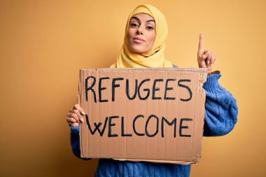 İslami başörtüsü takan güzel bir Arap kadın elinde mültecilerle bayrak tutuyor. Bir fikir ya da soruyla şaşırmış, mutlu yüzle işaret eden bir numaralı mesaj.