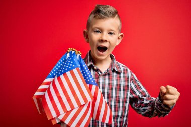 Küçük Amerikalı vatansever beyaz çocuk kırmızı arka planda bayrak sallayıp gururla zafer ve başarıyı kutluyor. Çok heyecanlı, coşkulu bir duygu.