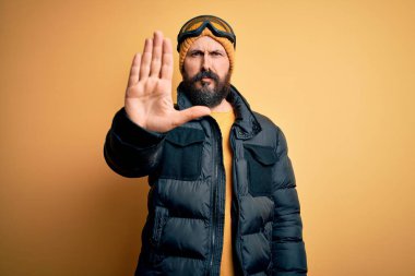 Sakallı, kar maskeli, kar maskeli ve kar gözlüklü yakışıklı kayakçı avucunun içi gibi şarkı söylemeyi kesiyor. Yüzünde olumsuz ve ciddi bir jest olan uyarı ifadesi.