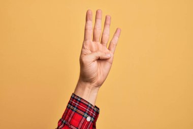 İzole edilmiş sarı arka planda parmaklarını gösteren beyaz bir gencin eli dört parmağı gösteriyor.