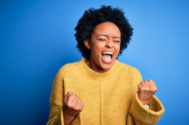 Sarı günlük kazak giyen kıvırcık saçlı, güzel Afro-Amerikan kadın kolları havada ve gözleri kapalı bir şekilde başarıyı kutluyor ve şaşırıyor. Kazanan konsept.