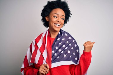 Kıvırcık saçlı, Amerika Birleşik Devletleri bayrağı takan genç Afrikalı Afro kadın gülümseyen bir gülümsemeyle baş parmağıyla işaret ediyor.