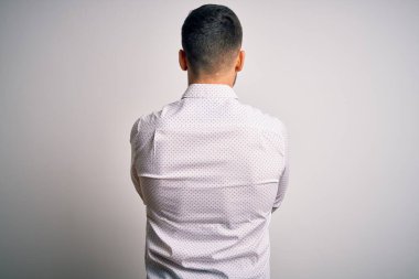 Zarif gömlekli genç adam izole edilmiş beyaz arka planda dikilip kollarını kavuşturup arkana bakıyor.